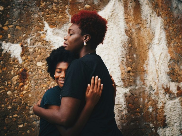 Black mother hugging her child against a wall