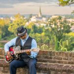 A Black elder sitting on a brick wall playing a guitar. Finally living life his way.