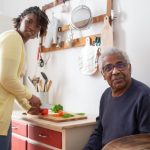 Black Lady Caregiver assisting an older Black man.