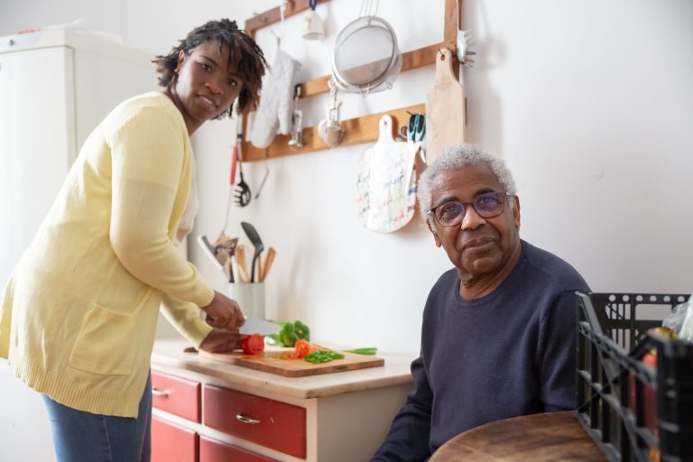 Black Lady Caregiver assisting an older Black man.
